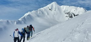 4 skiers skiing on a snow covered slope with a large alpine snow covered mountain in the background in the Chugach Mountains